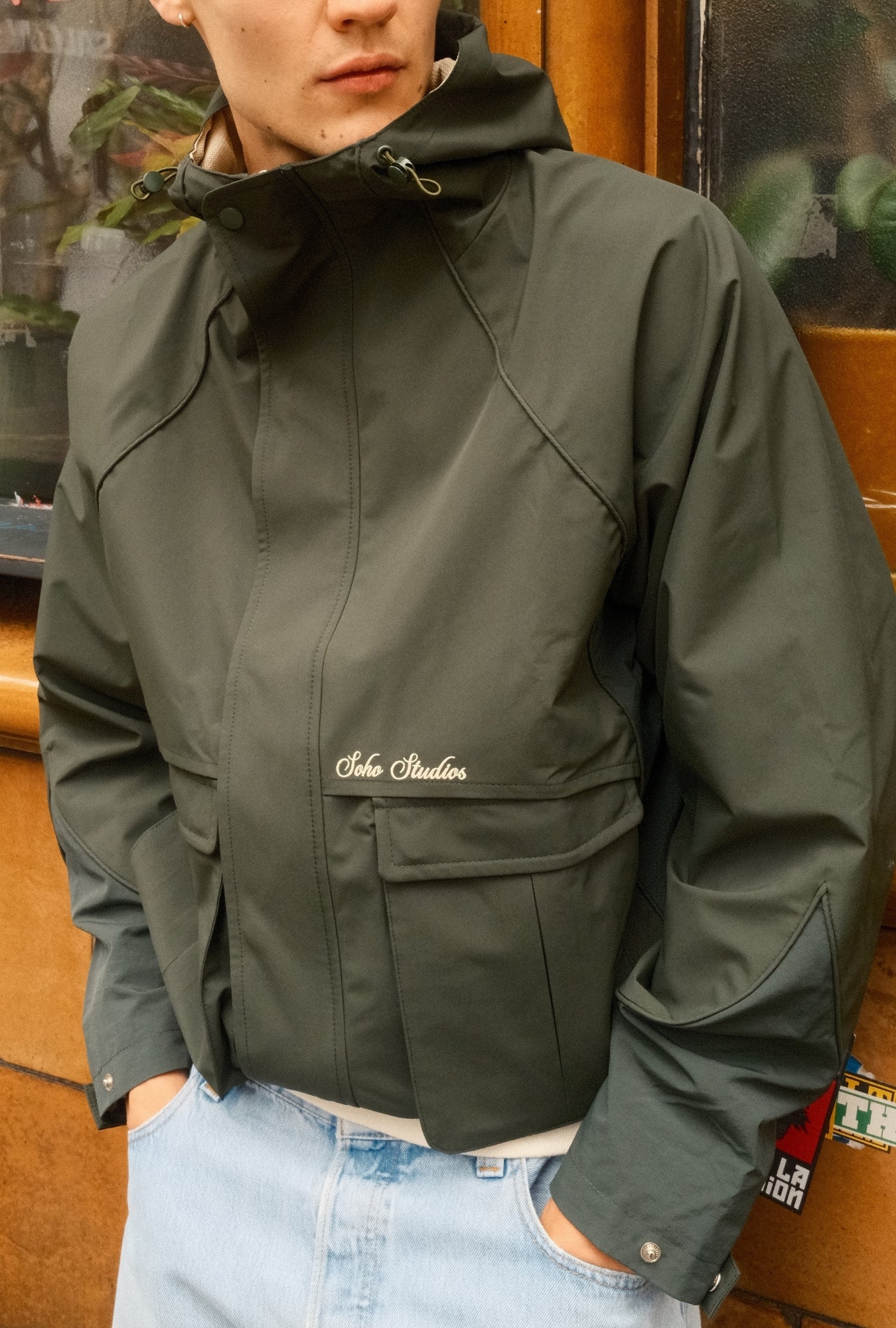 Person wearing a dark green jacket with a brand logo, standing indoors.