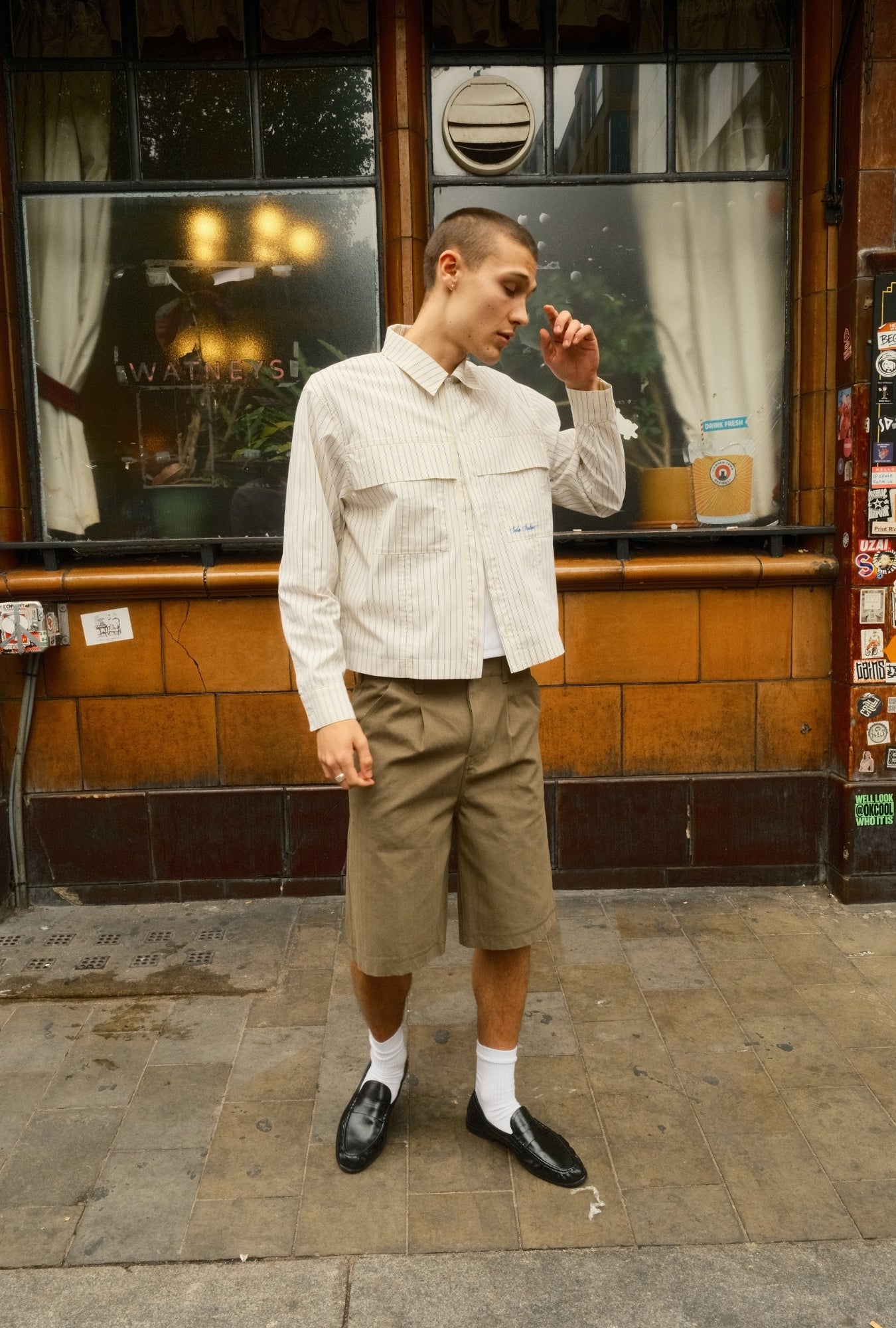 Man standing in front of a store with a tiled wall and window display.
