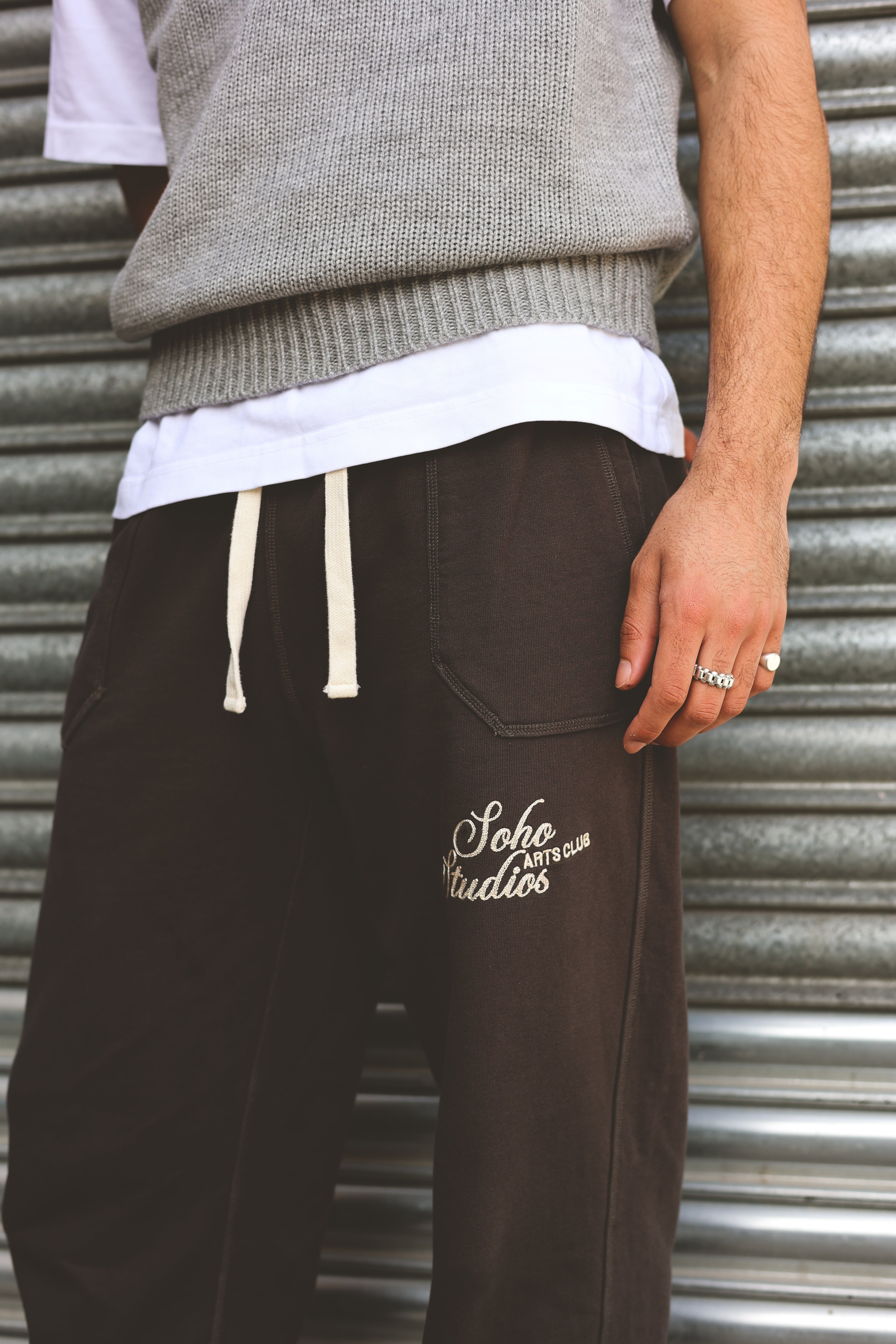 Person wearing brown sweatpants with 'Soho Studios' logo against a metal shutter background