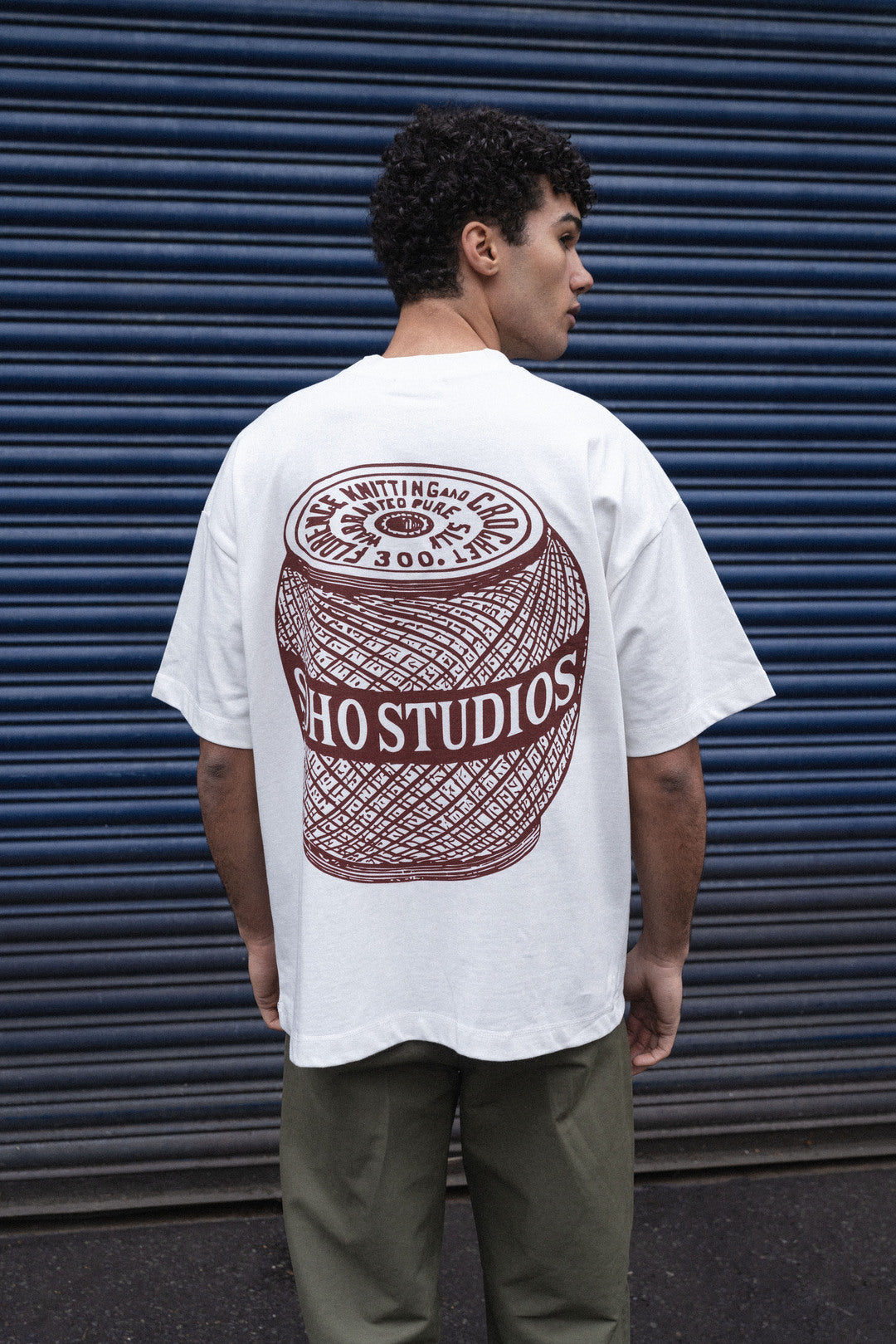 Men wearing a white t-shirt with a burgundy screen printed logo on the back that reads 'SOHO STUDIOS' and a date '2008'.