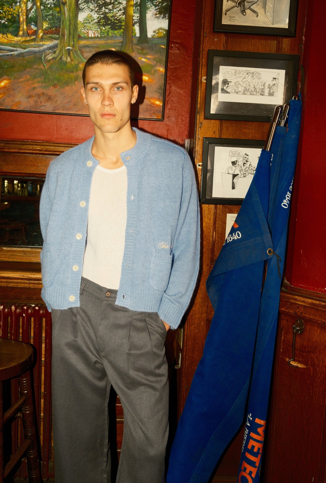 Man wearing a blue cardigan in a room with wooden walls and framed pictures.