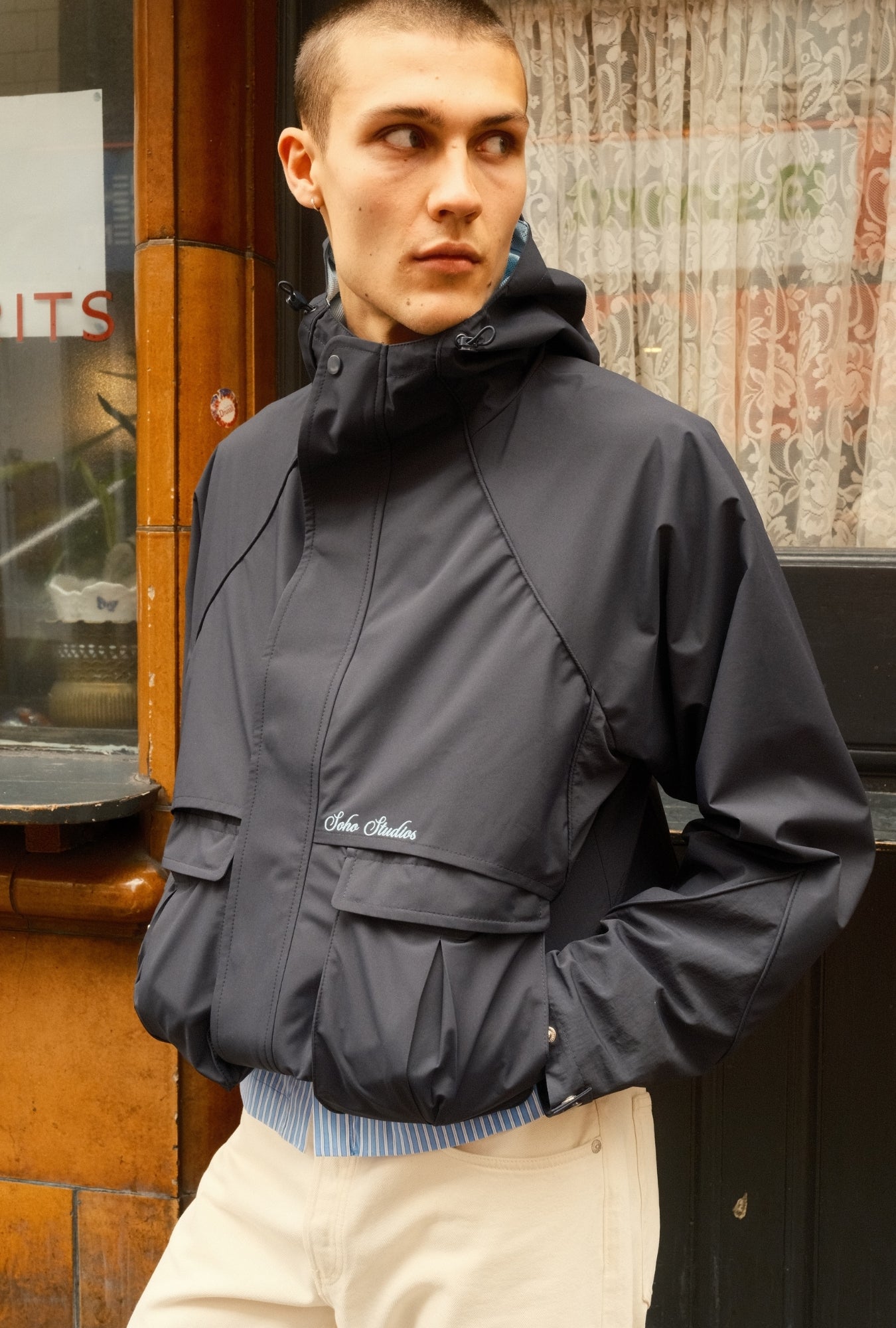 Person wearing a dark gray jacket with a brand logo, standing in front of a store entrance.