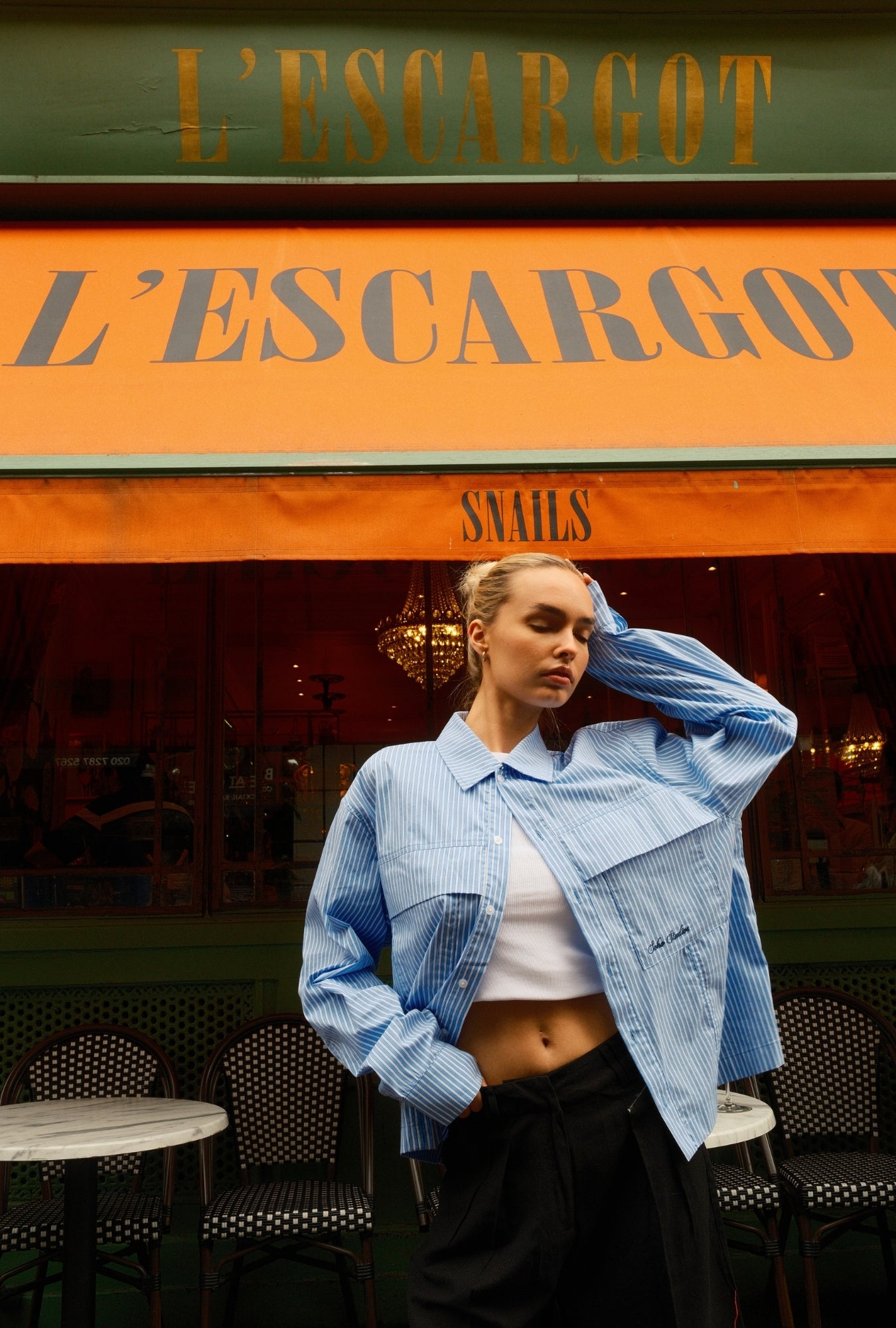 Woman in a blue jacket standing in front of an 'L'Escargot' restaurant.