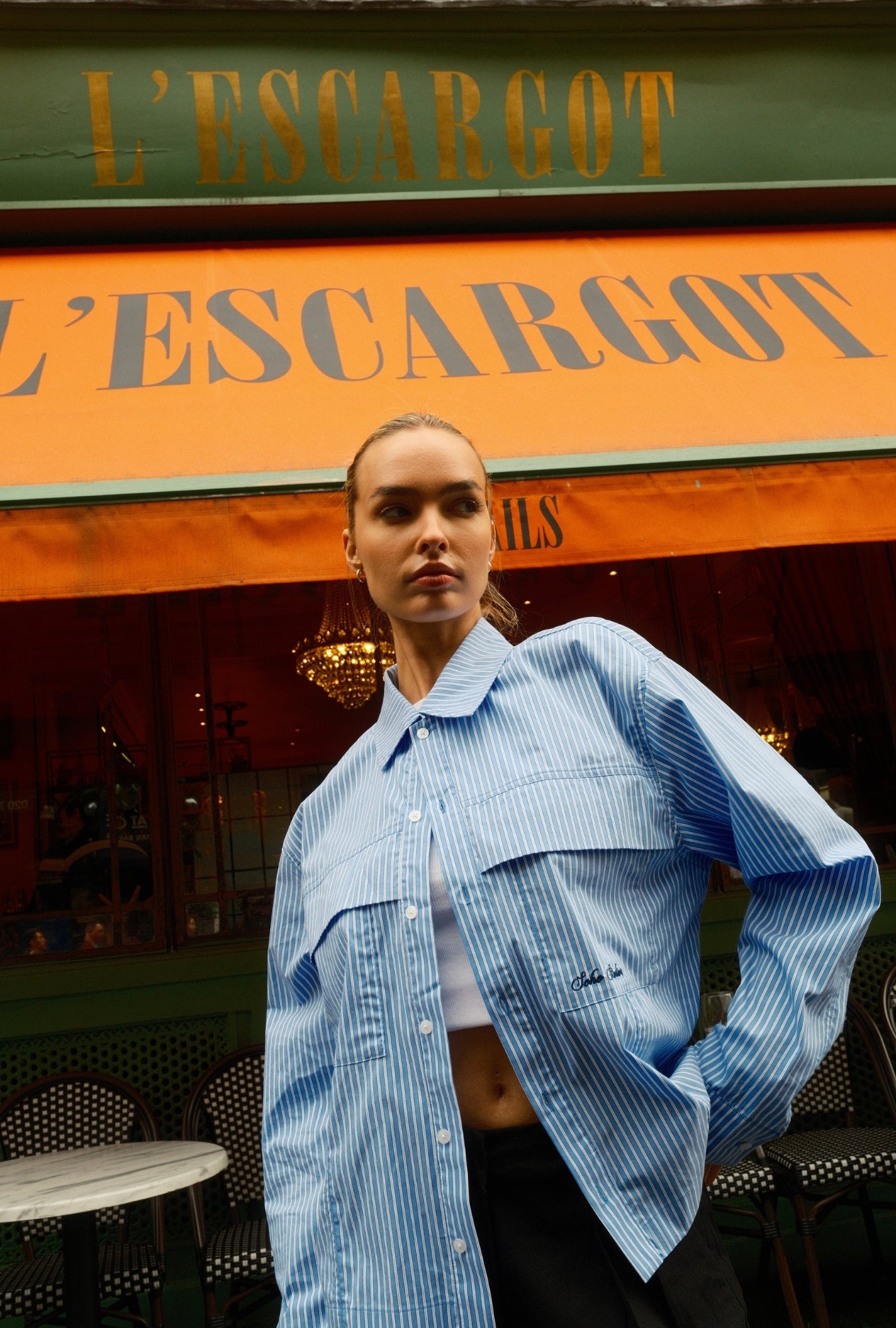 Woman wearing oversized blue striped button-up shirt outside café storefront