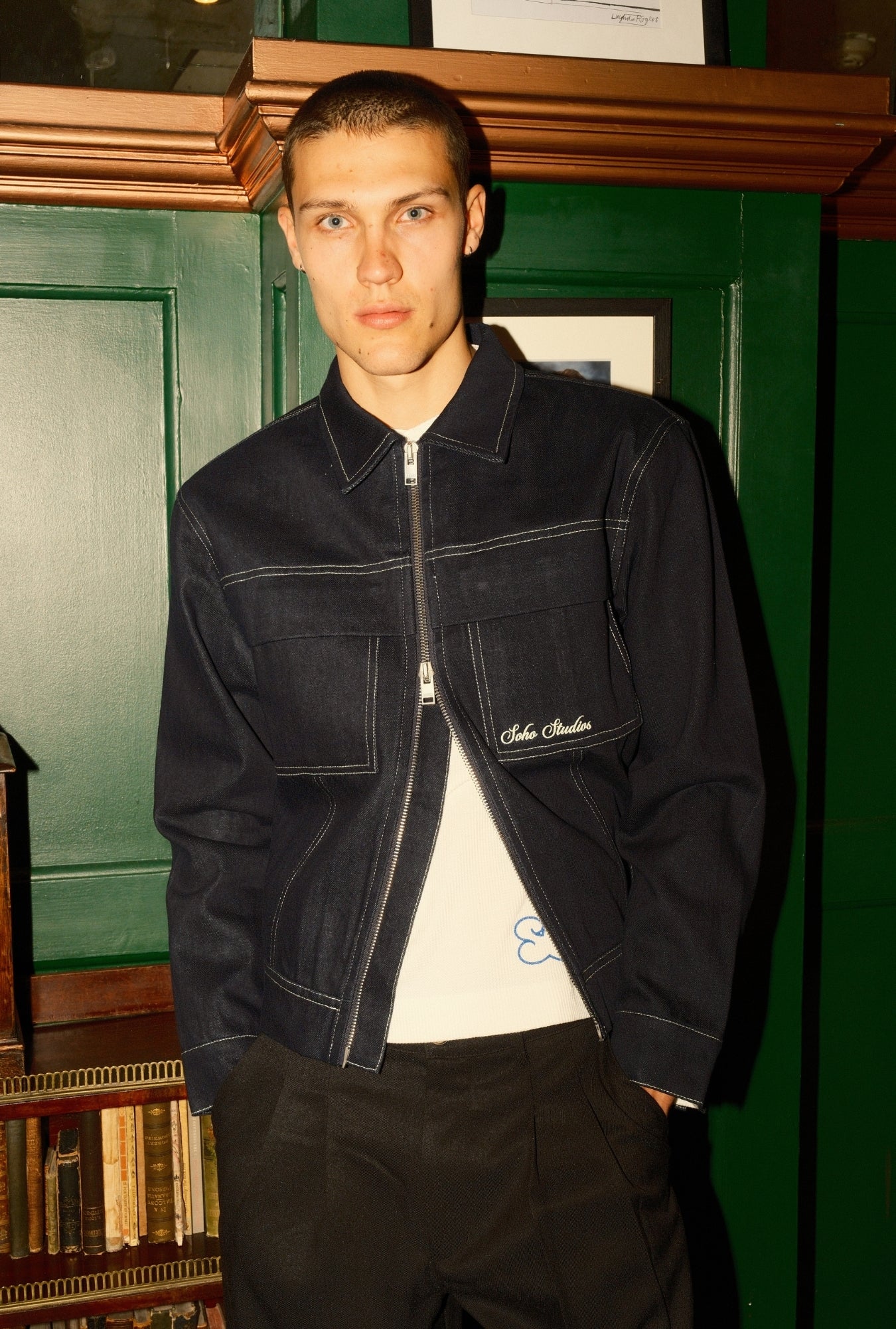 Man wearing a dark jacket with a visible brand logo against a green wall.