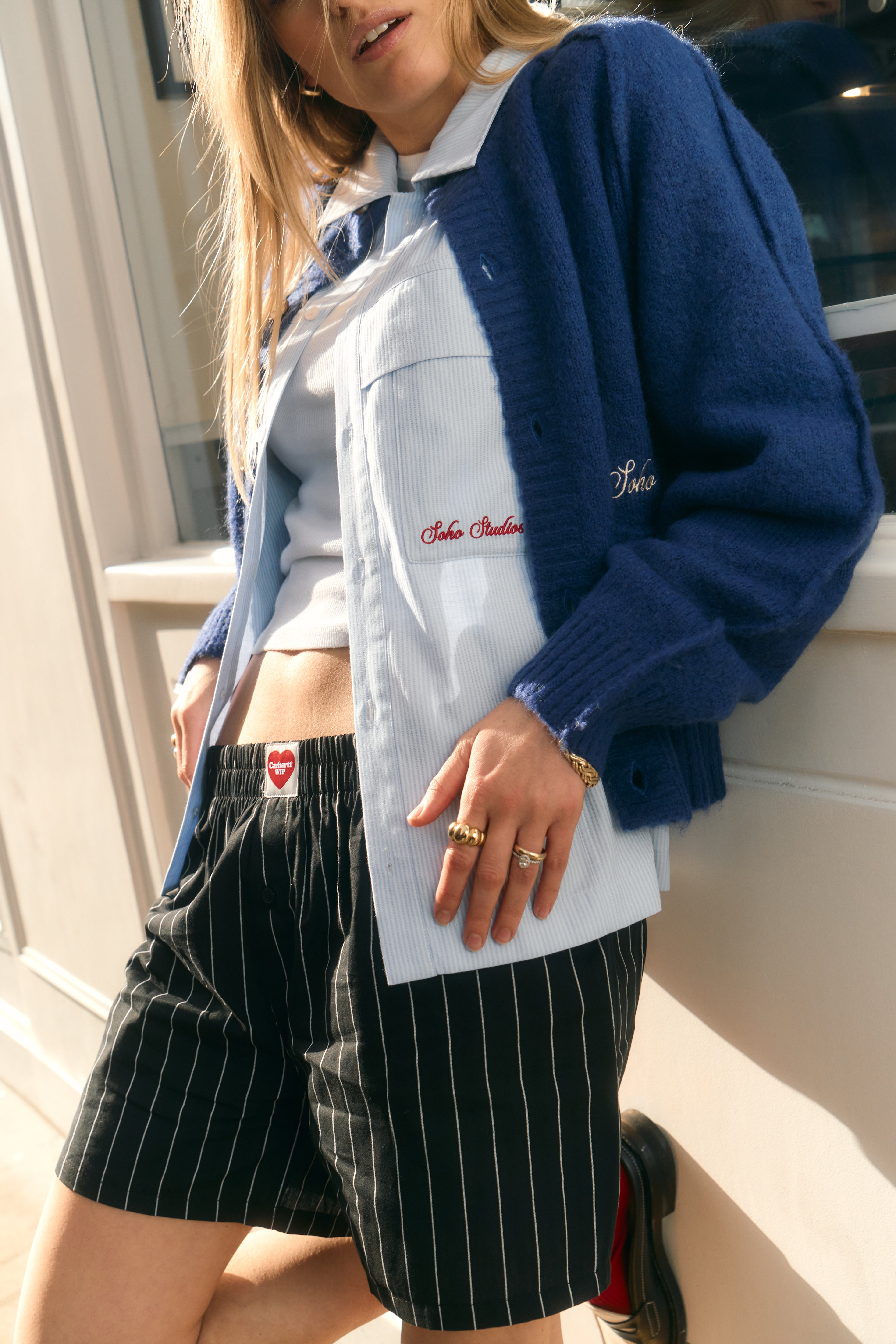 Woman wearing blue cardigan, striped shorts and loafers inside retro-style outdoor interior