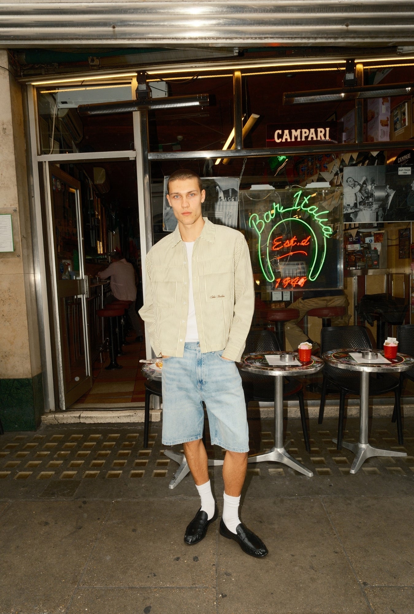 Man standing outside a bar with neon signs, including Campari and Bar Bolo.