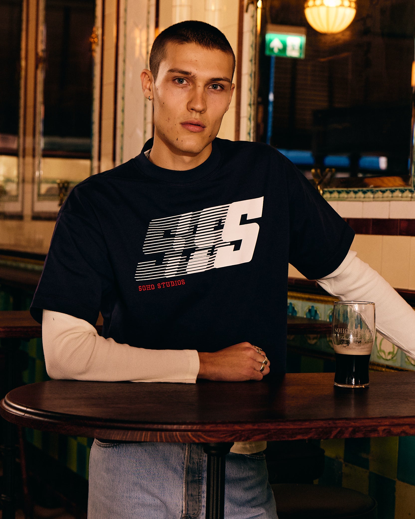 Man wearing a black sweatshirt with a Soho Studio logo in a bar setting