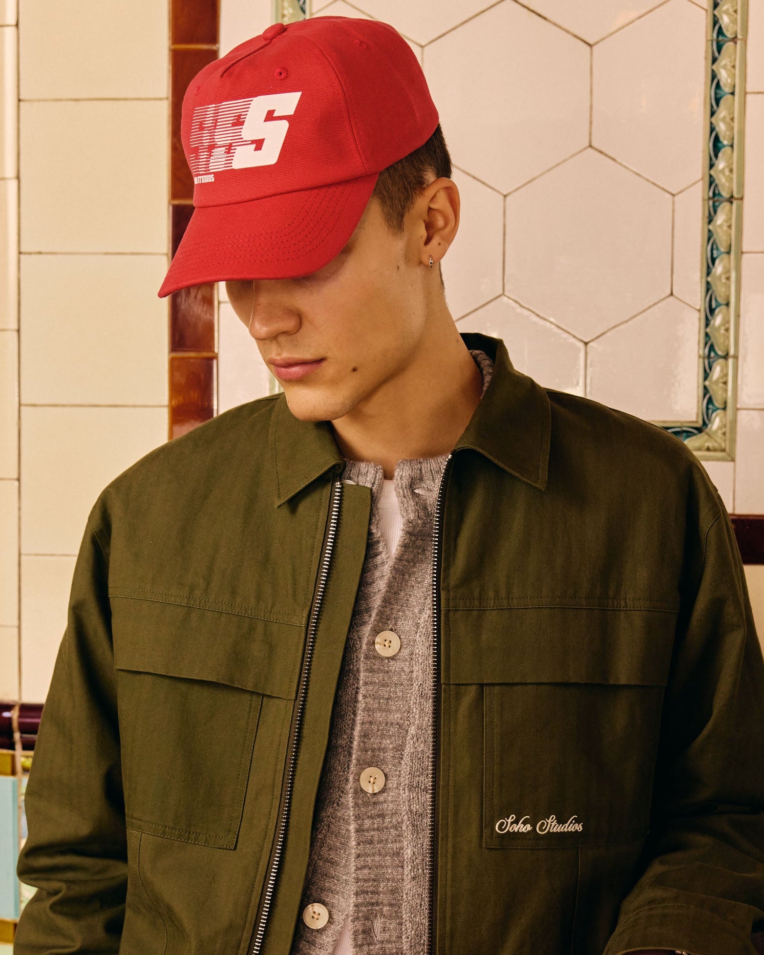 Man wearing a red cap and green jacket in a tiled room