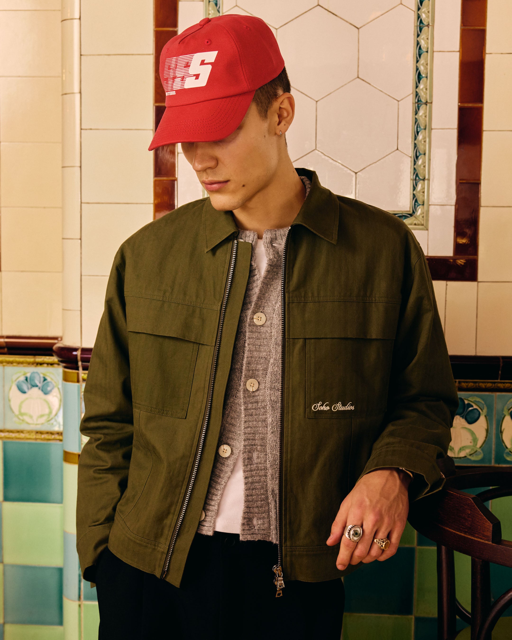 Man wearing a red cap and green jacket in a tiled room