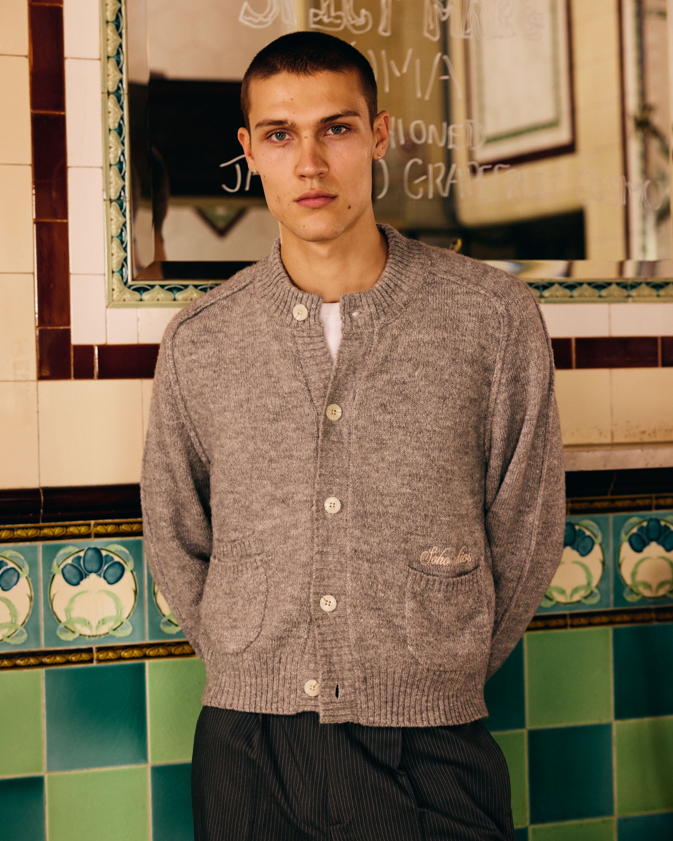 Man wearing a gray cardigan in a bathroom with tiled walls