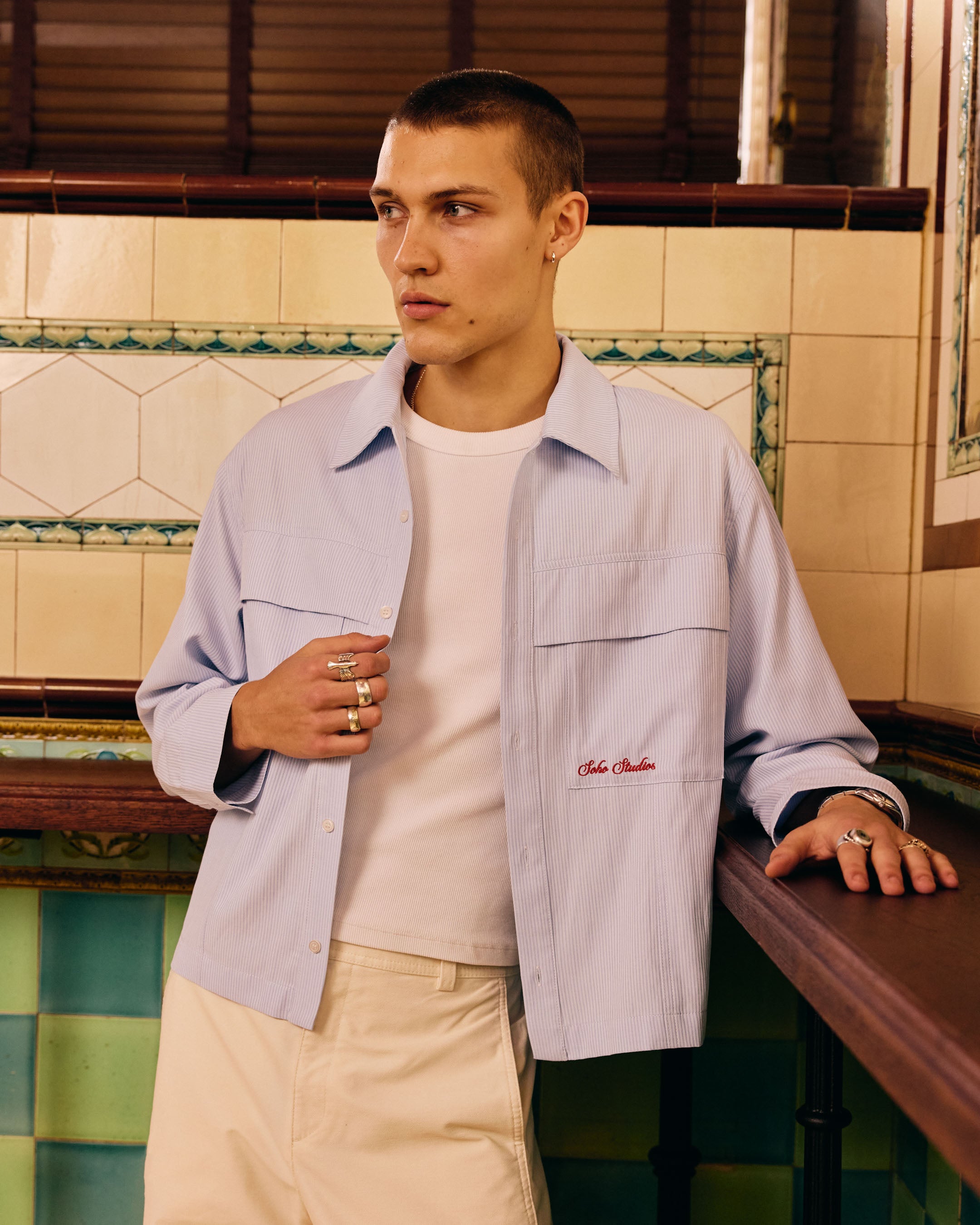 Man wearing a light blue jacket with a Soho Studio logo, standing in a tiled room.