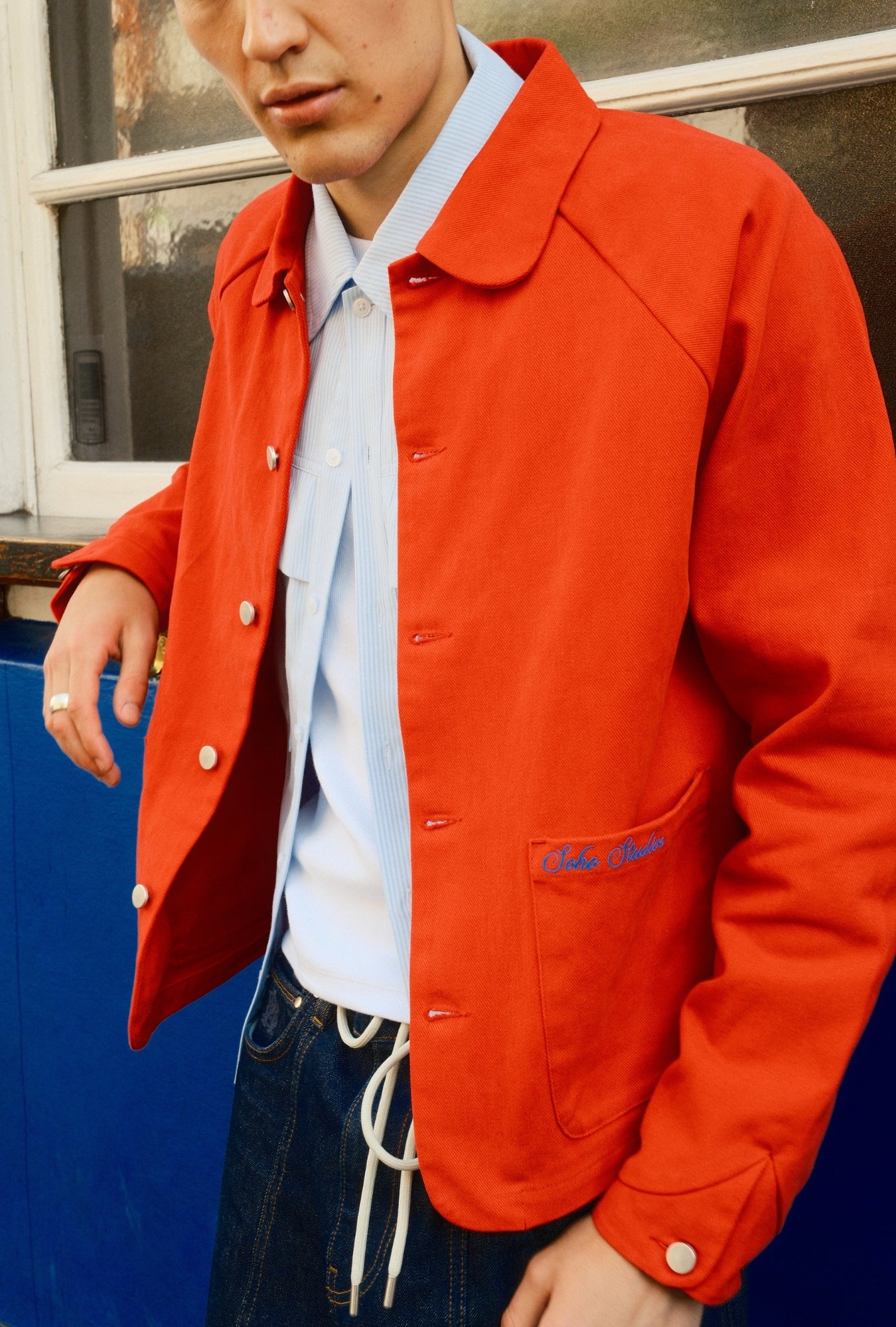Person wearing a red jacket with a brand logo, standing against a blue and white background.