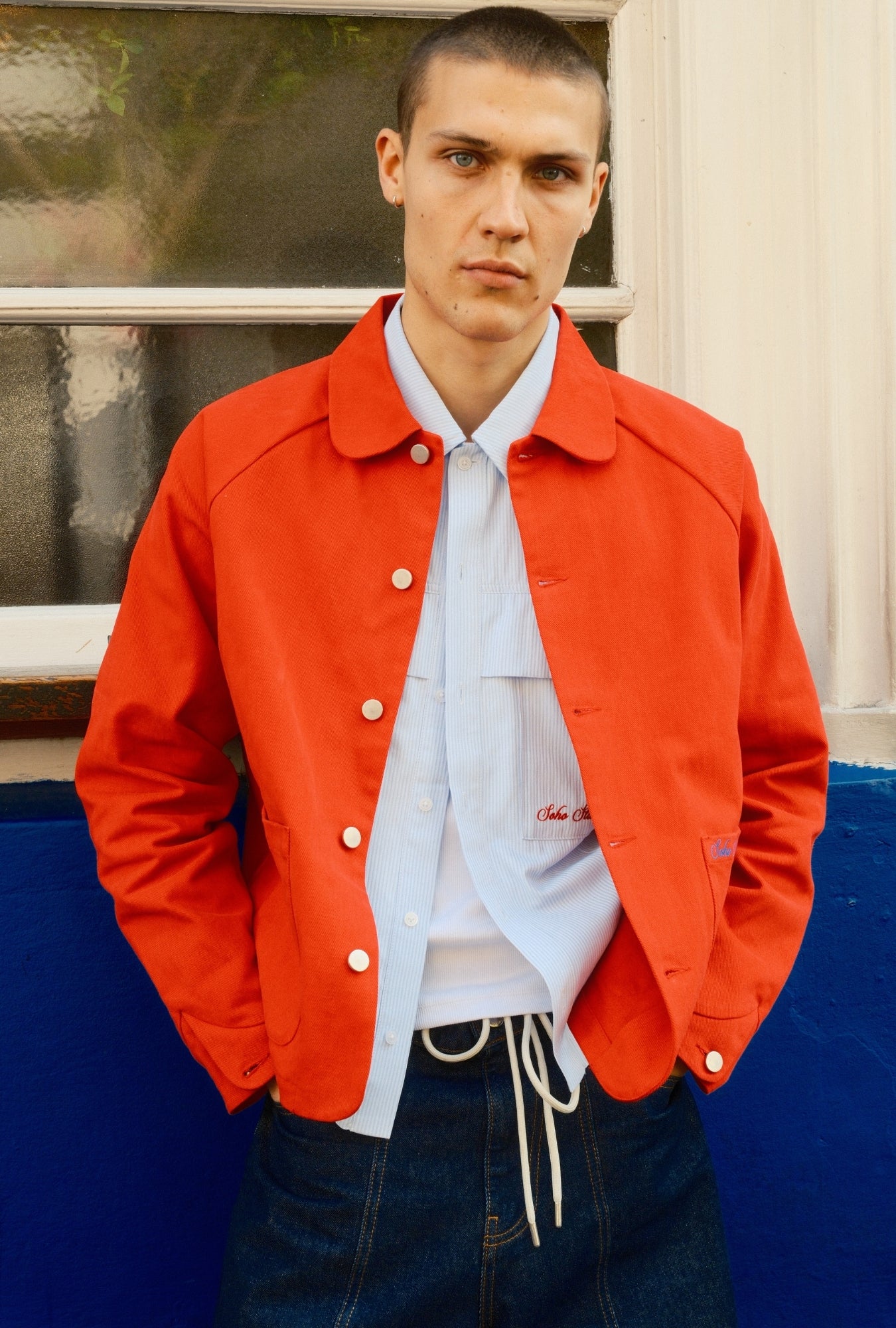 Person wearing a bright red jacket over a white shirt with text, standing outdoors.