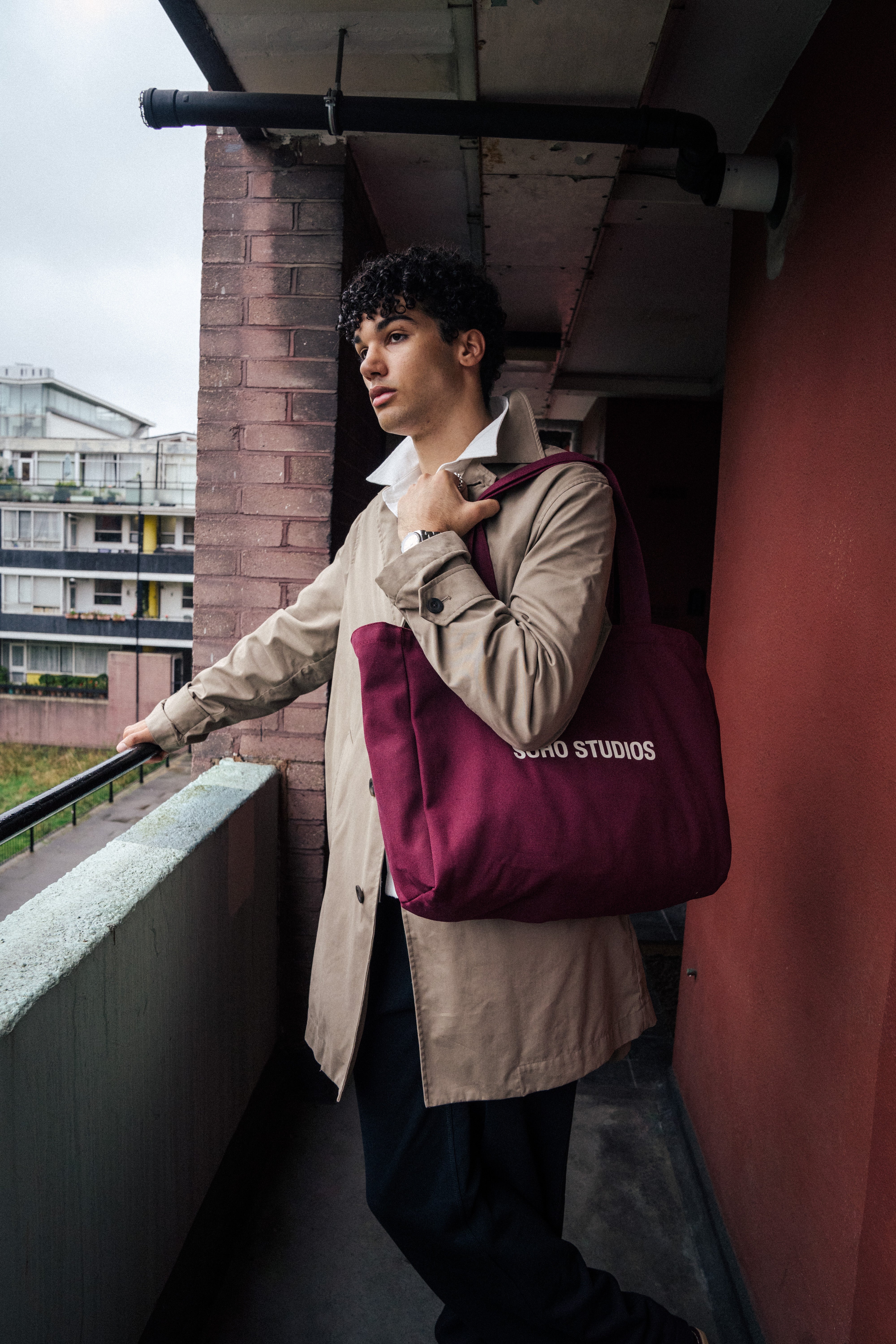 Man carrying burgundy Soho Studios tote bag with beige trench coat outdoors