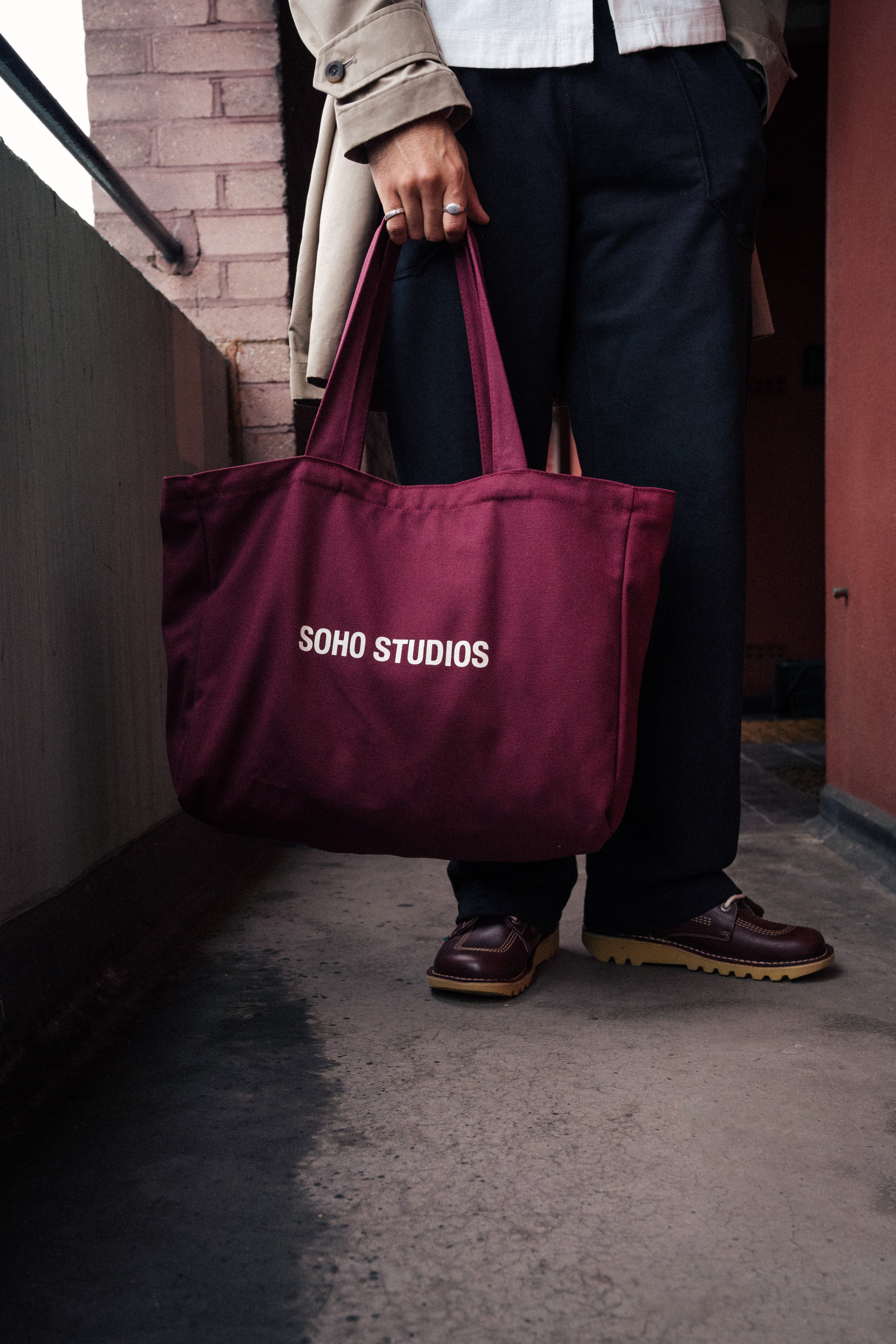 Man carrying burgundy Soho Studios tote bag with black pent outdoors
