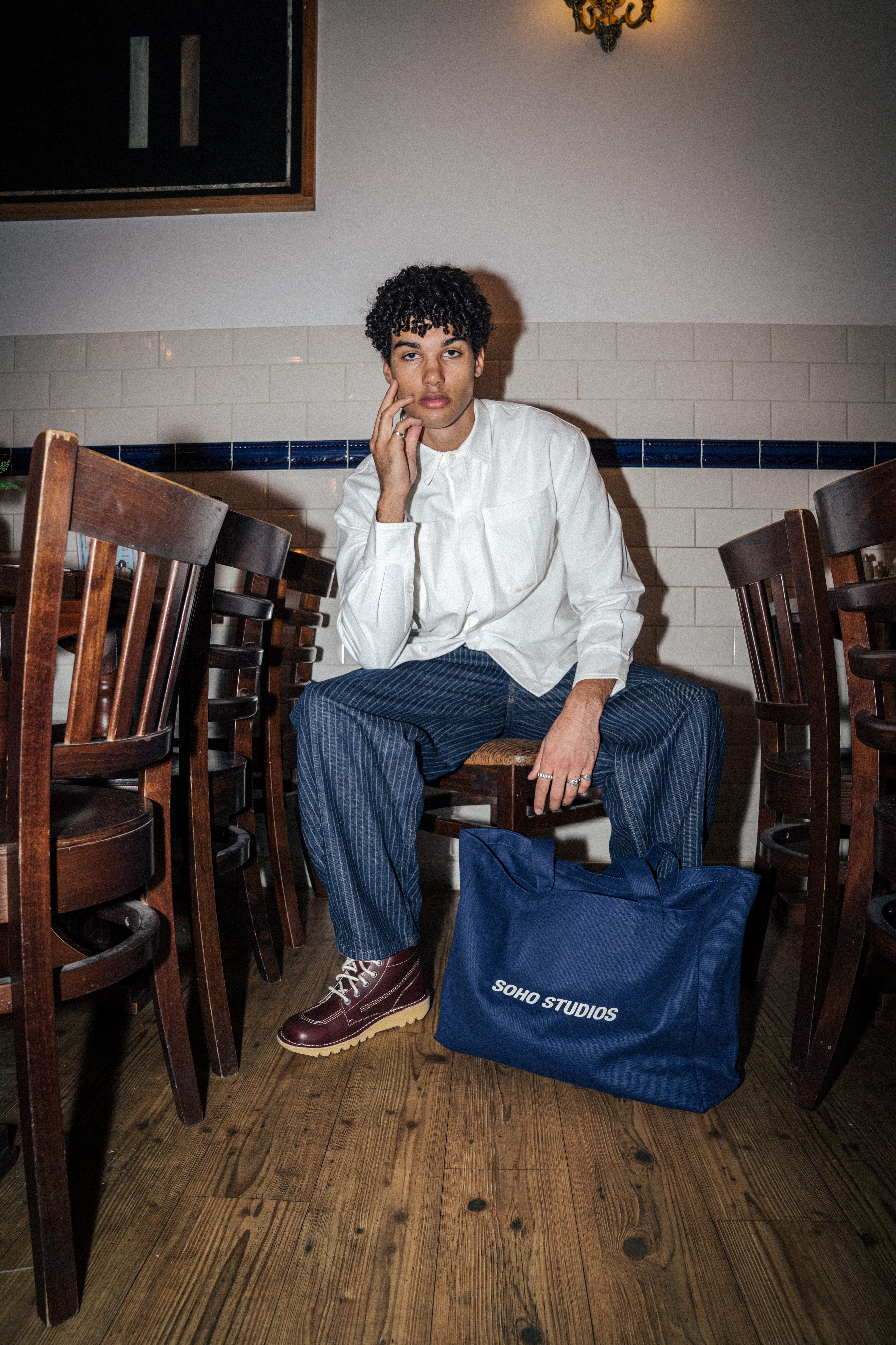 Men sitting along with NAVY TOTE BAG on wood chairs with a white tiles background 