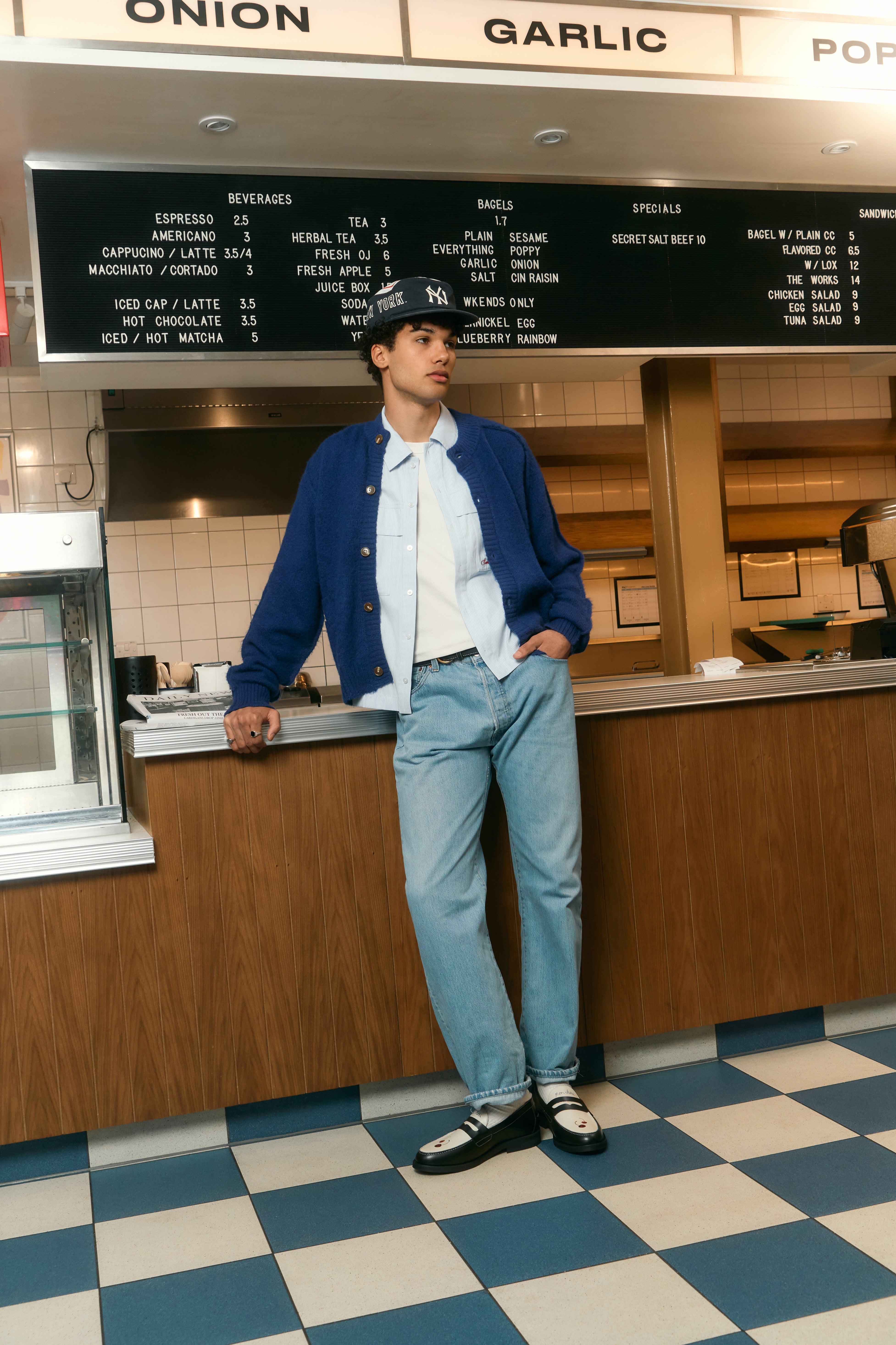 A person wearing a royal blue alpaca cardigan with a boxy silhouette, standing in a room with a counter and menu in the background.