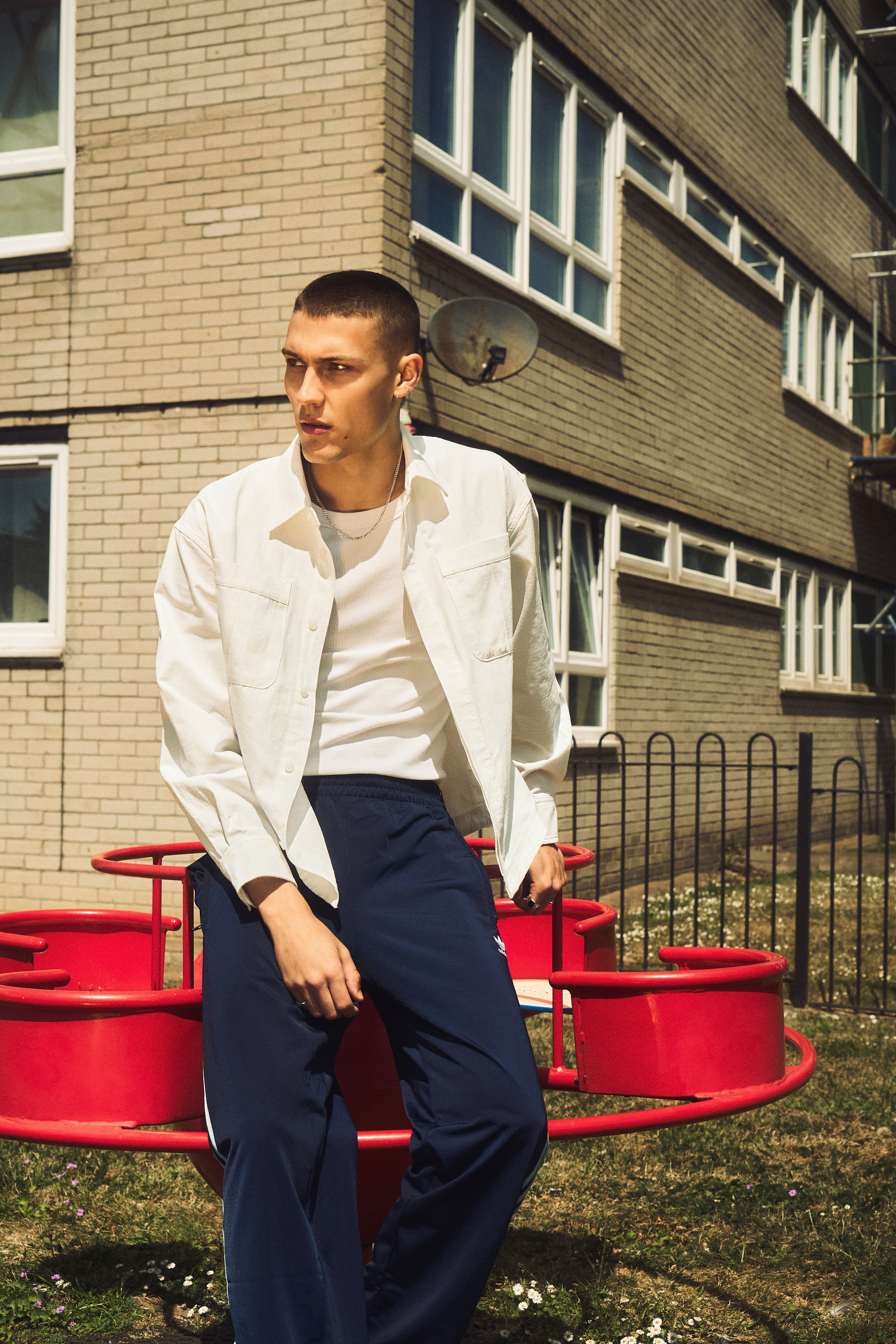 Man in a white shirt and blue pants sitting on a red metal structure in front of a brick building.