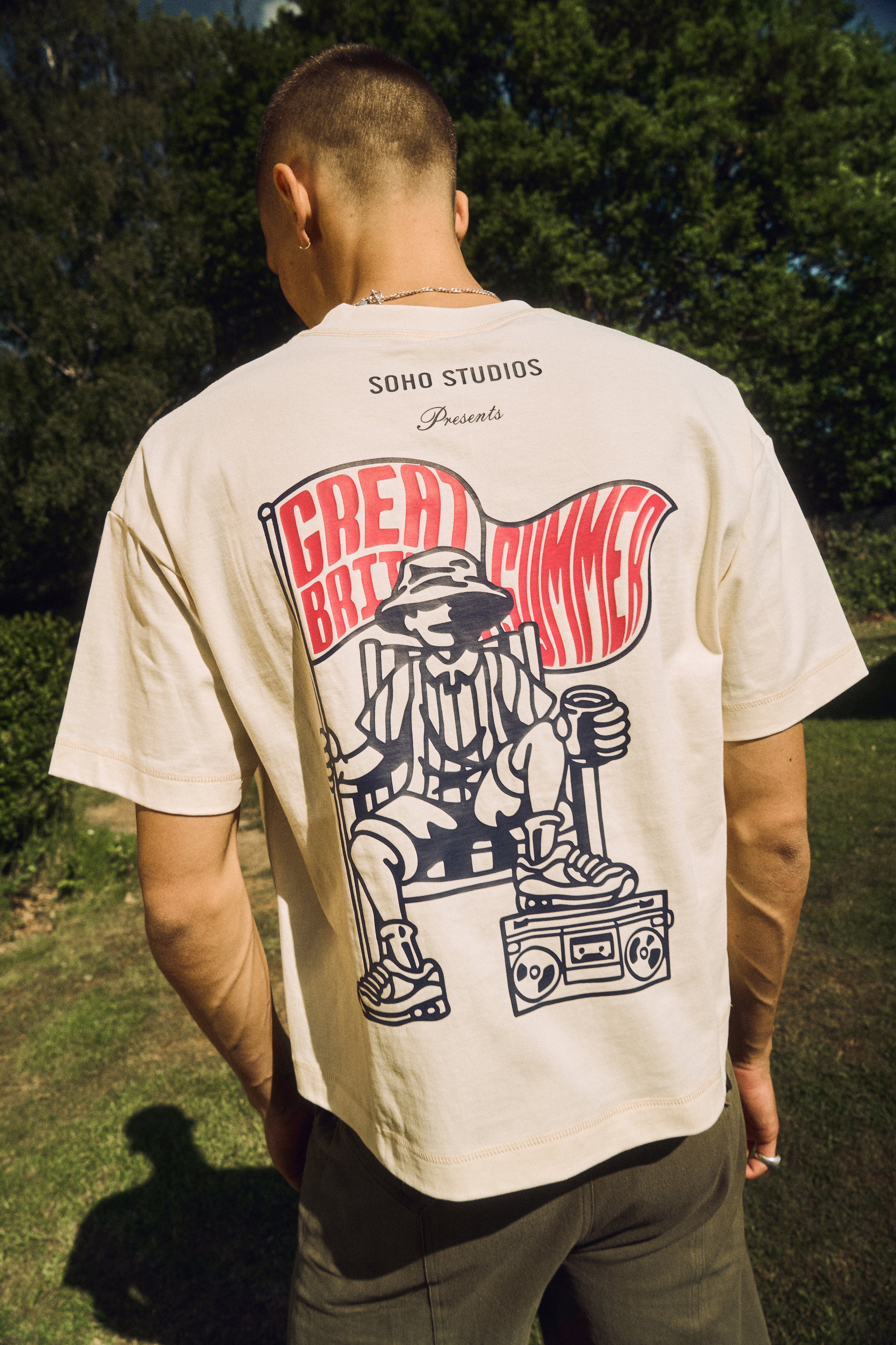 Person wearing a beige t-shirt with a graphic design on the back, standing outdoors.