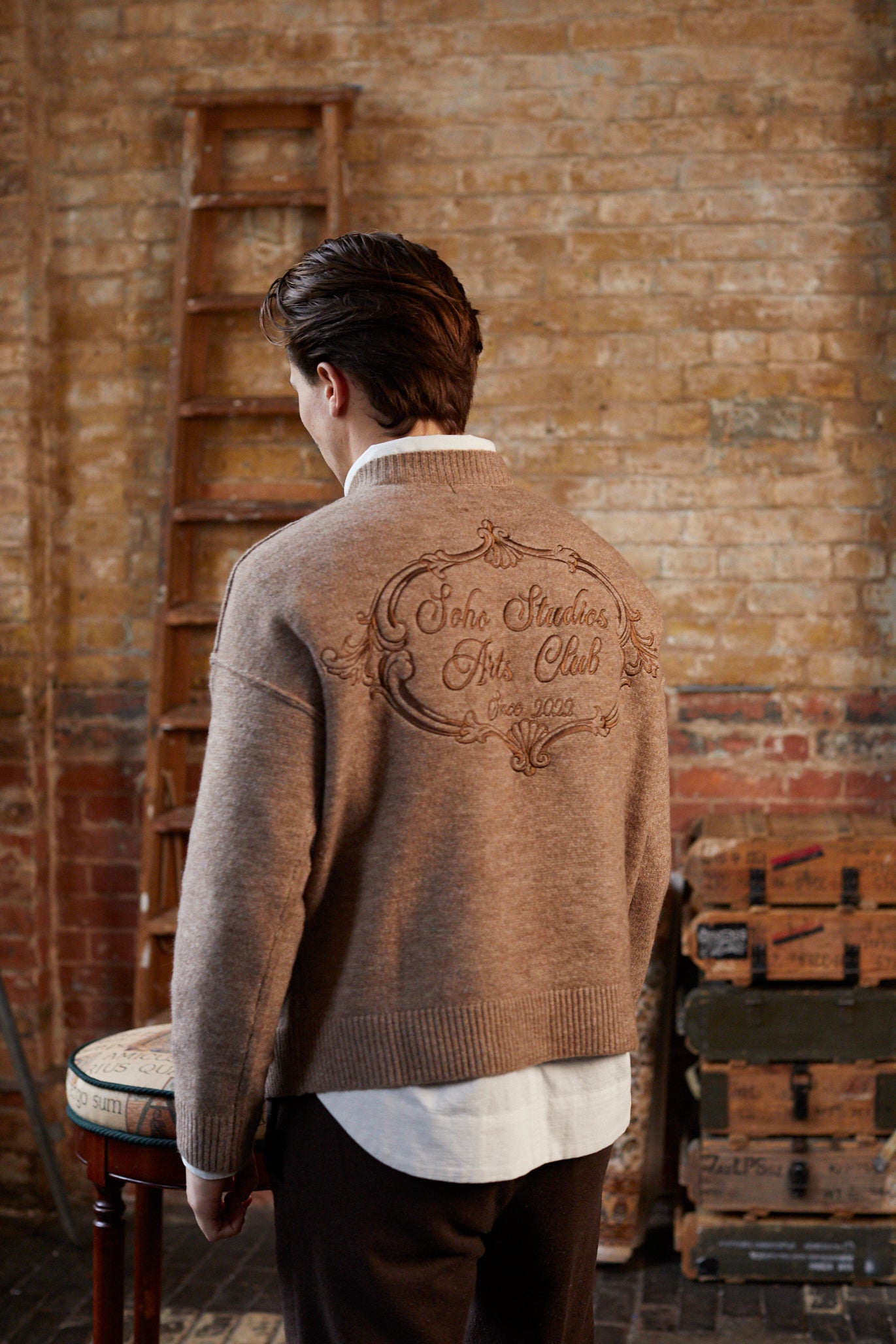 Man wearing a brown sweater with embroidery in a rustic setting