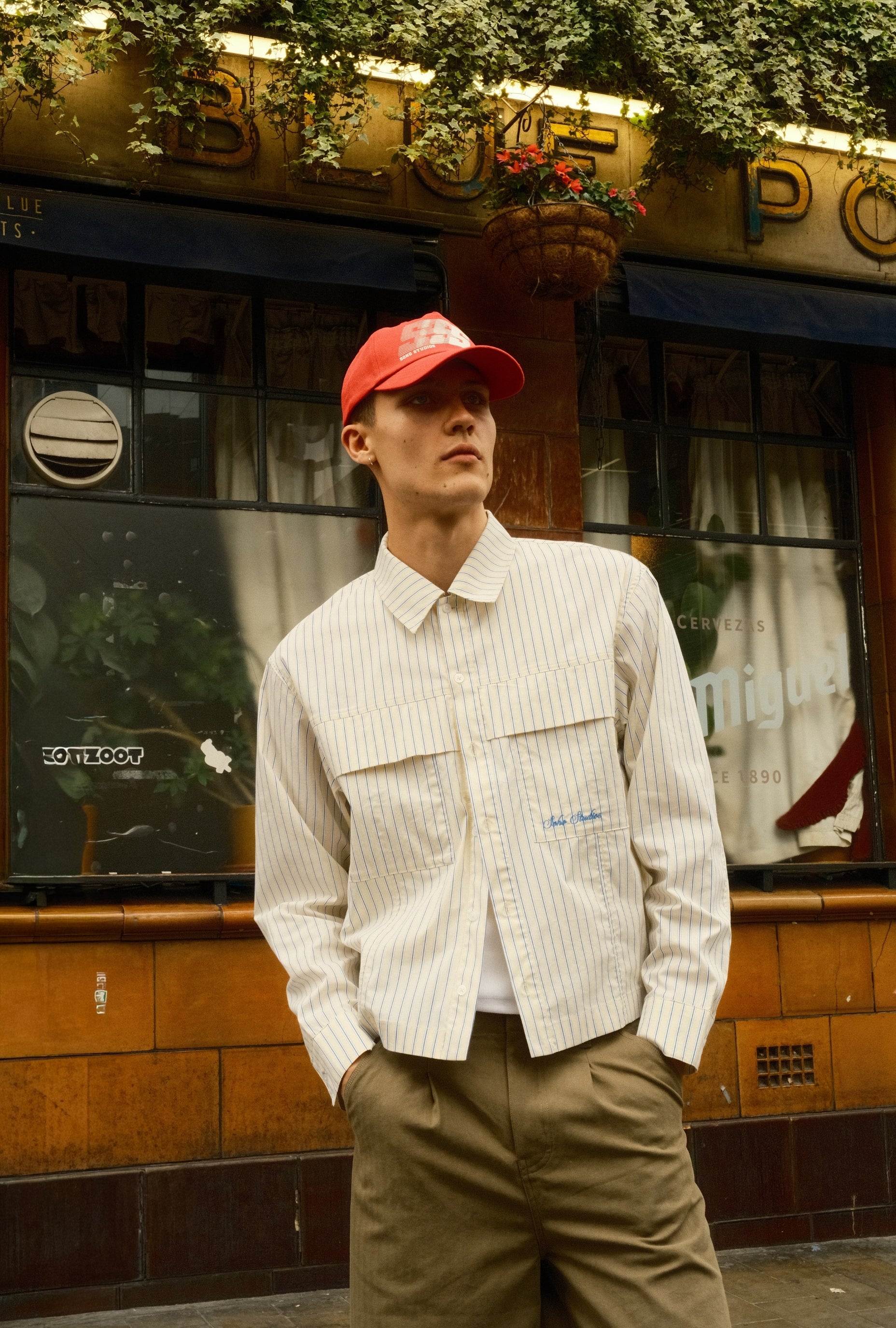 Person wearing a white striped shirt and red cap standing in front of a vintage building.