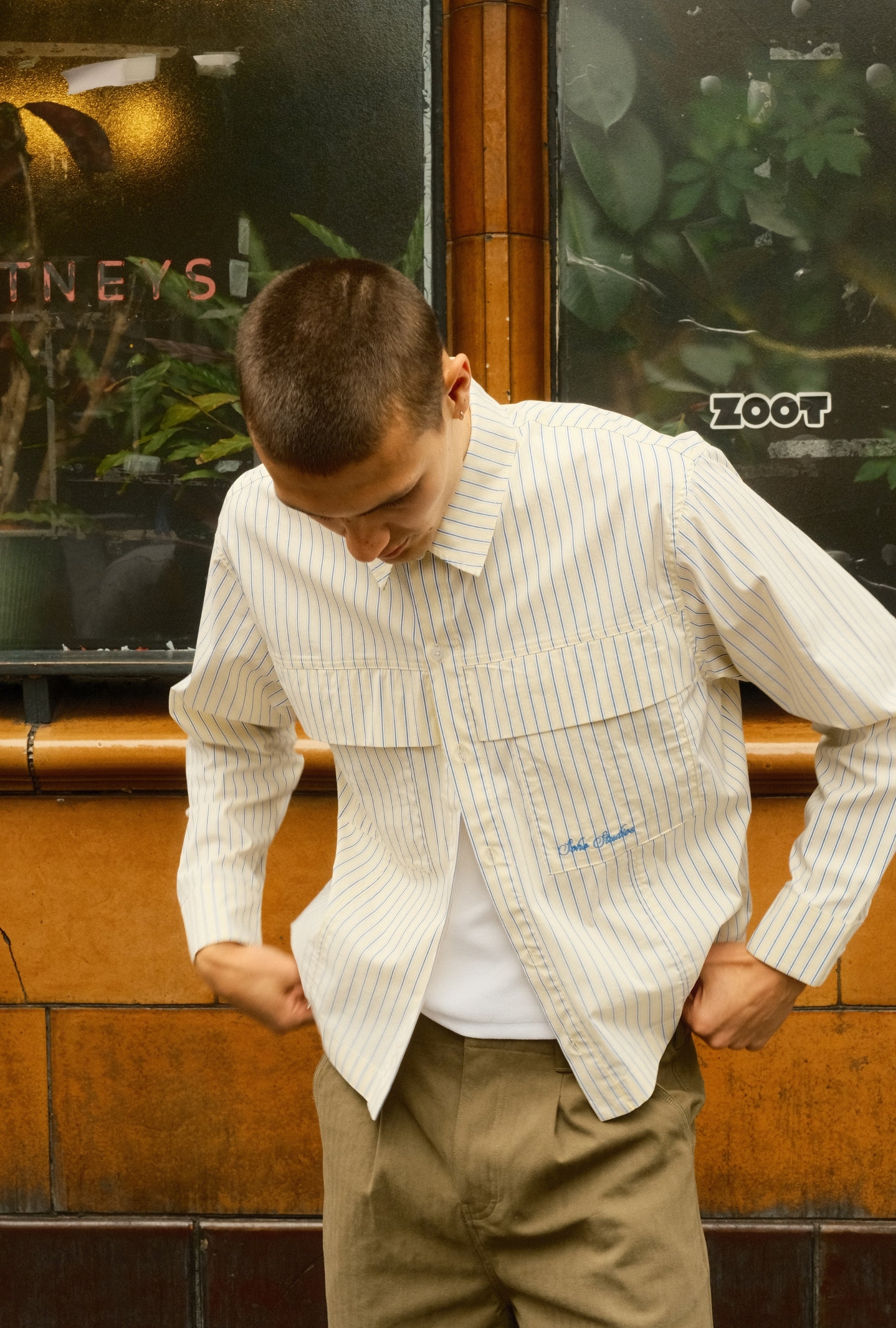 Man wearing a striped shirt over a vest with 'Soho Studip' branding in an outdoor setting.